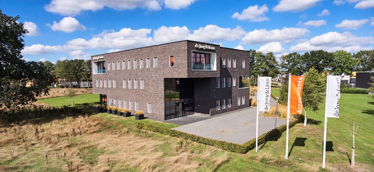 Bruin pand met daaromheen gras en vlaggen is van de Jong en Laan vestiging Hardenberg